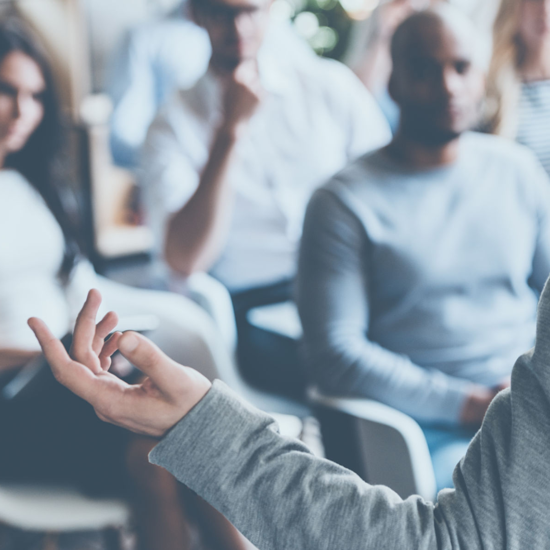 A speaker gesturing to an engaged audience in a conference setting.