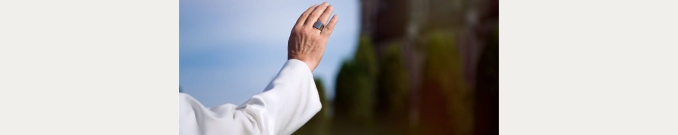 A hand raised in a gesture of greeting against a blurred background.