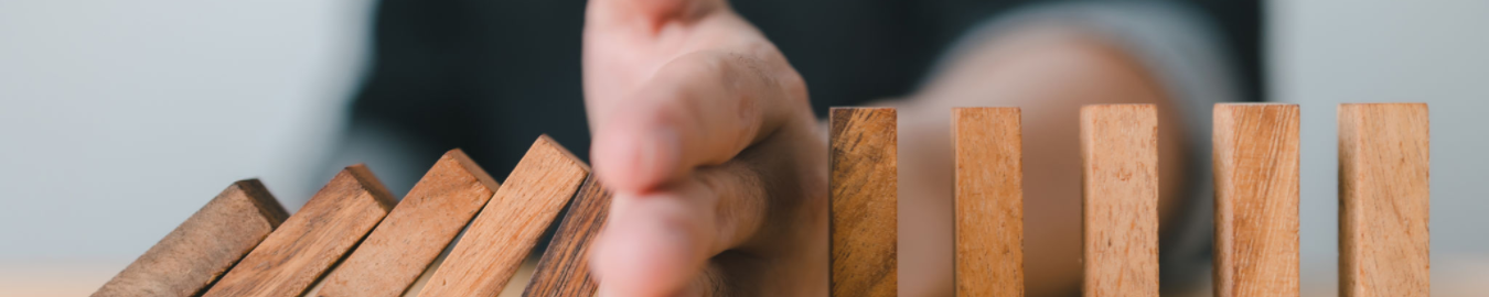 Geopolitics for Enterprise Risk Management A hand stopping wooden blocks from falling in a domino effect.